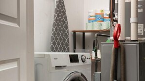 A laundry area with a front-loading washing machine, a red vacuum cleaner, and a wall-mounted ironing board. - Flexhome East Village • Modern 2BR • Quiet Street (Chicago)
