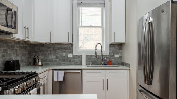 A modern kitchen with white cabinets, a stainless steel refrigerator, a built-in oven, and a window above the sink. - Flexhome East Village • Modern 2BR • Quiet Street (Chicago)