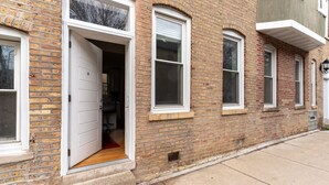 A two-story brick building with a white door open to a wooden interior. - Flexhome East Village • Modern 2BR • Quiet Street (Chicago)