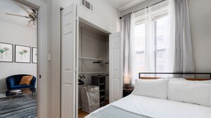 Une chambre à coucher avec un lit, une armoire, une chaise et une fenêtre avec des rideaux.