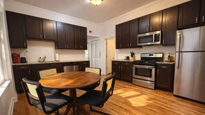 Une cuisine moderne avec des meubles de rangement en bois foncé, des appareils électroménagers en acier inoxydable et une table ronde en bois, assortie de chaises.