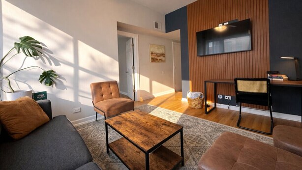 Un salon moderne comprenant un canapé, un fauteuil, une table basse et un téléviseur fixé à un mur en bois.
