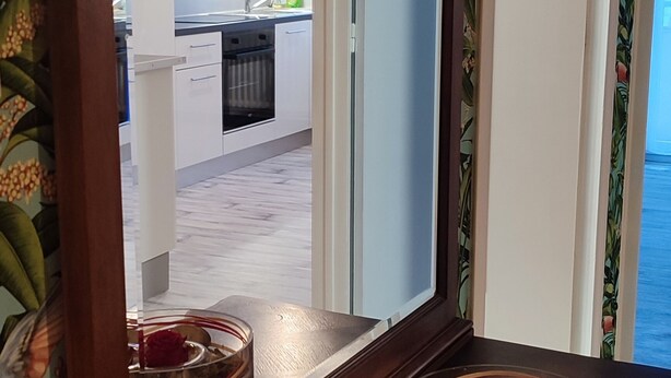 A wooden console table with decorative bowls and a mirror reflecting a kitchen area.