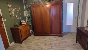 A hallway with a wooden wardrobe, a small wooden cabinet, and a door with a green wall and floral wallpaper.