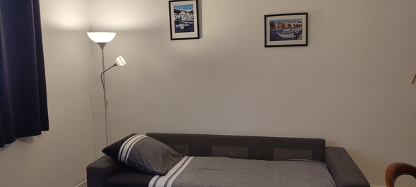 A bedroom with a bed, a floor lamp, and two framed pictures on the wall.