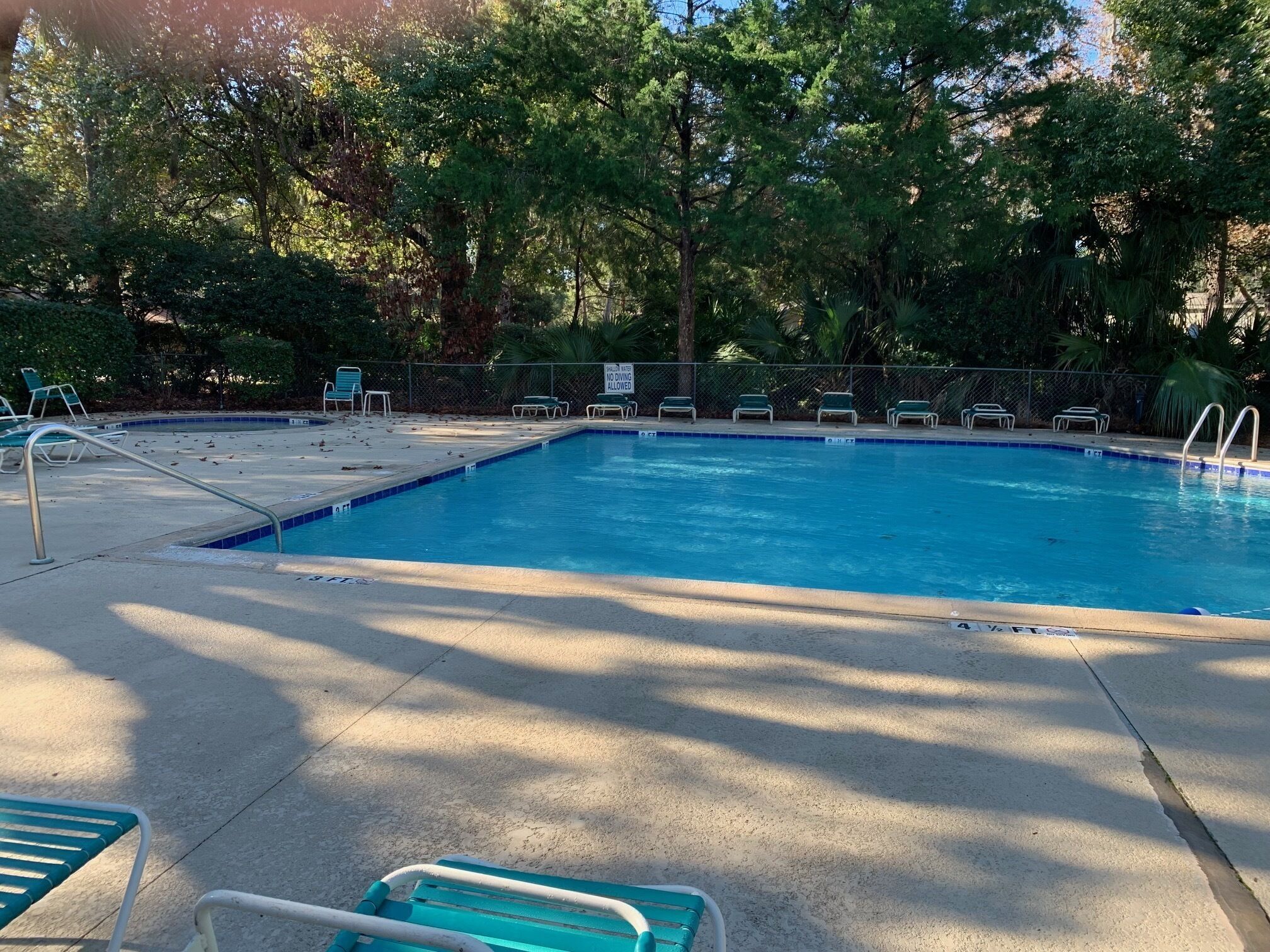 A swimming pool with a tiled edge, surrounded by green chairs and a fence.