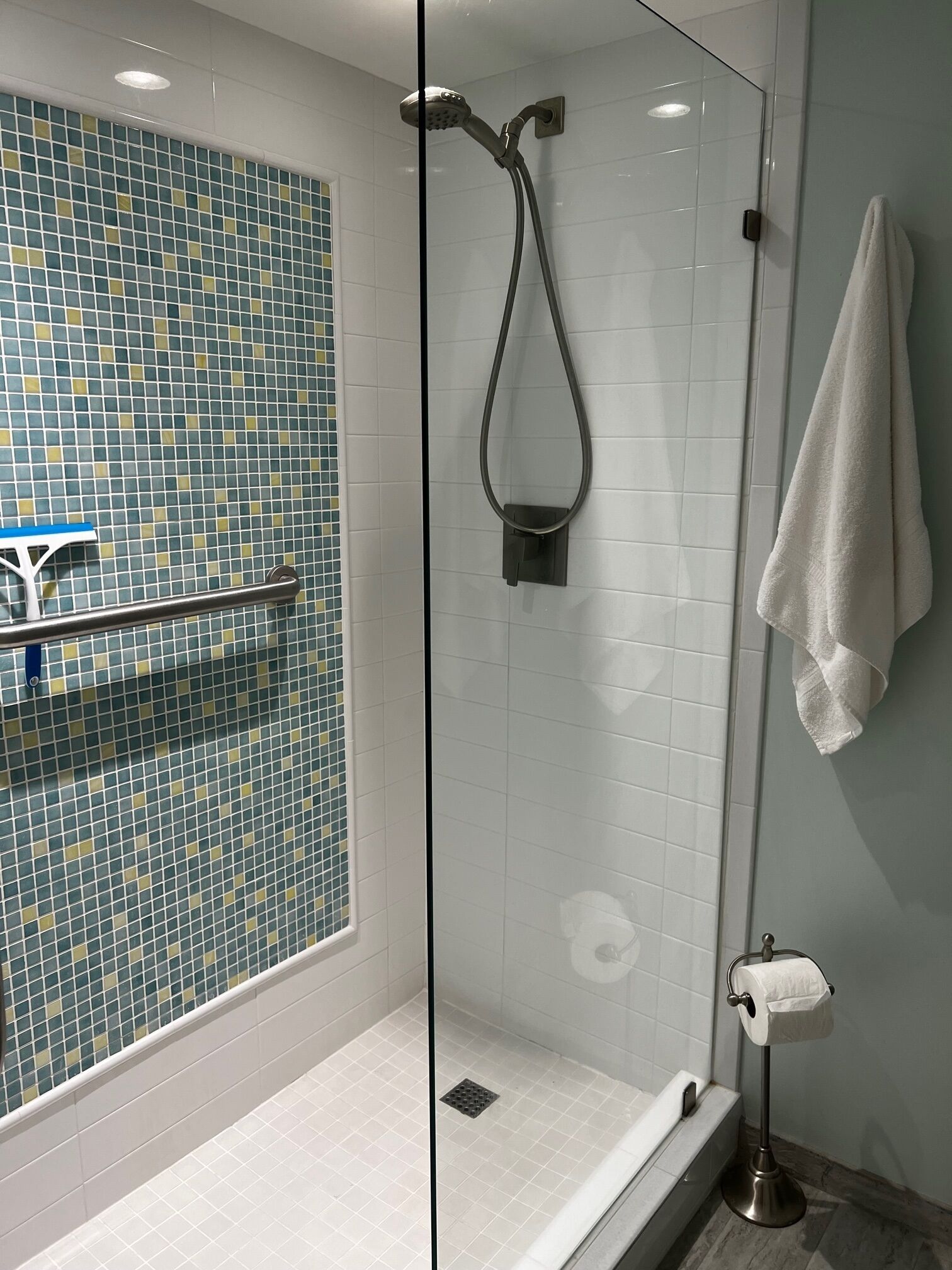 Ein modernes Badezimmer mit einer gläsernen Duschkabine, einer weißen Badewanne und einer mit blau-gelbem Muster versehenen Wand.