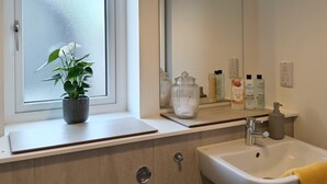 A bathroom with a window, a sink, a mirror, and toiletries on the counter.
