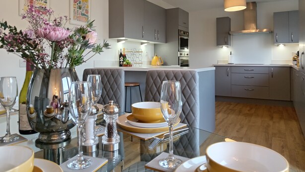 A modern kitchen with grey cabinetry, a central island, and a dining area with a glass table set for a meal.