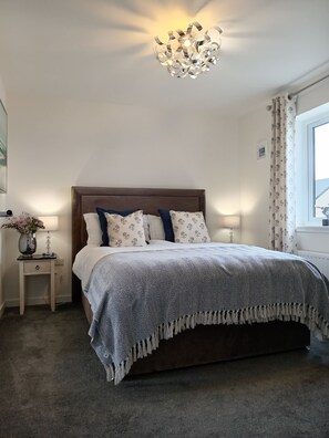 Une chambre à coucher avec un grand lit, une table de chevet avec une lampe, un luminaire décoratif au plafond et une fenêtre avec des rideaux.
