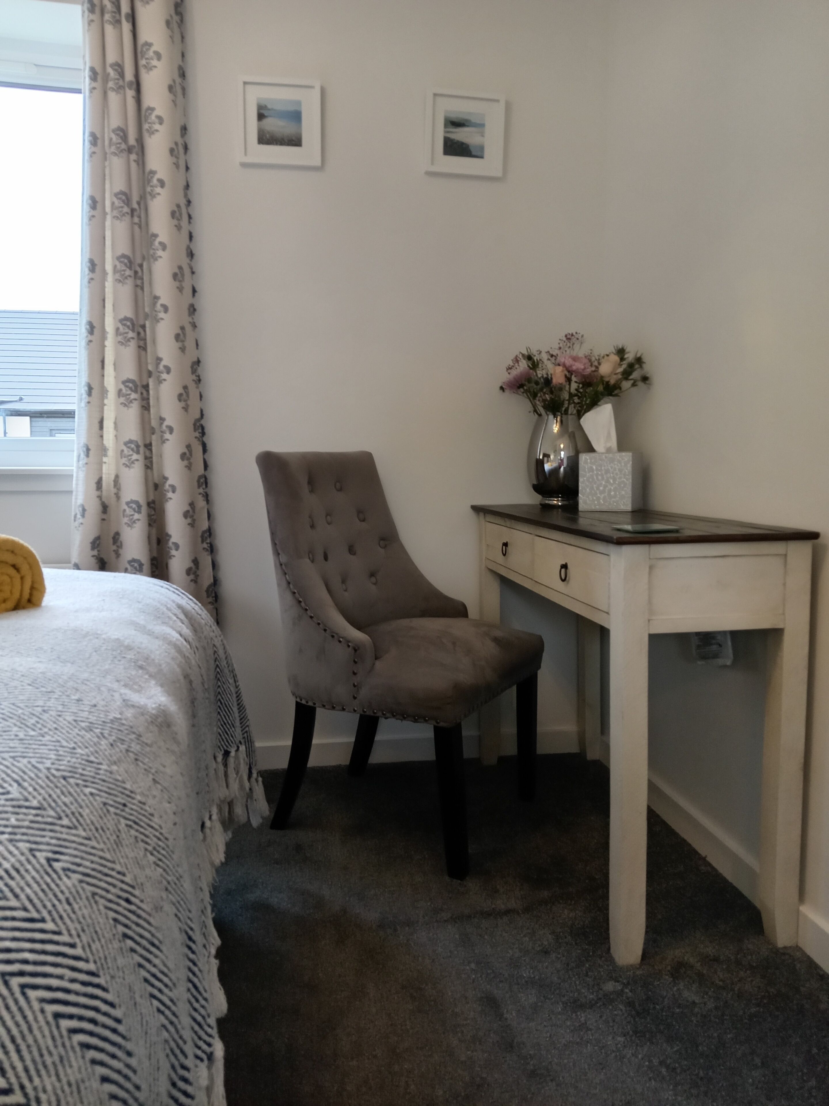 Ein Schlafzimmer mit Bett, Stuhl, Schreibtisch und einer Blumenvase.