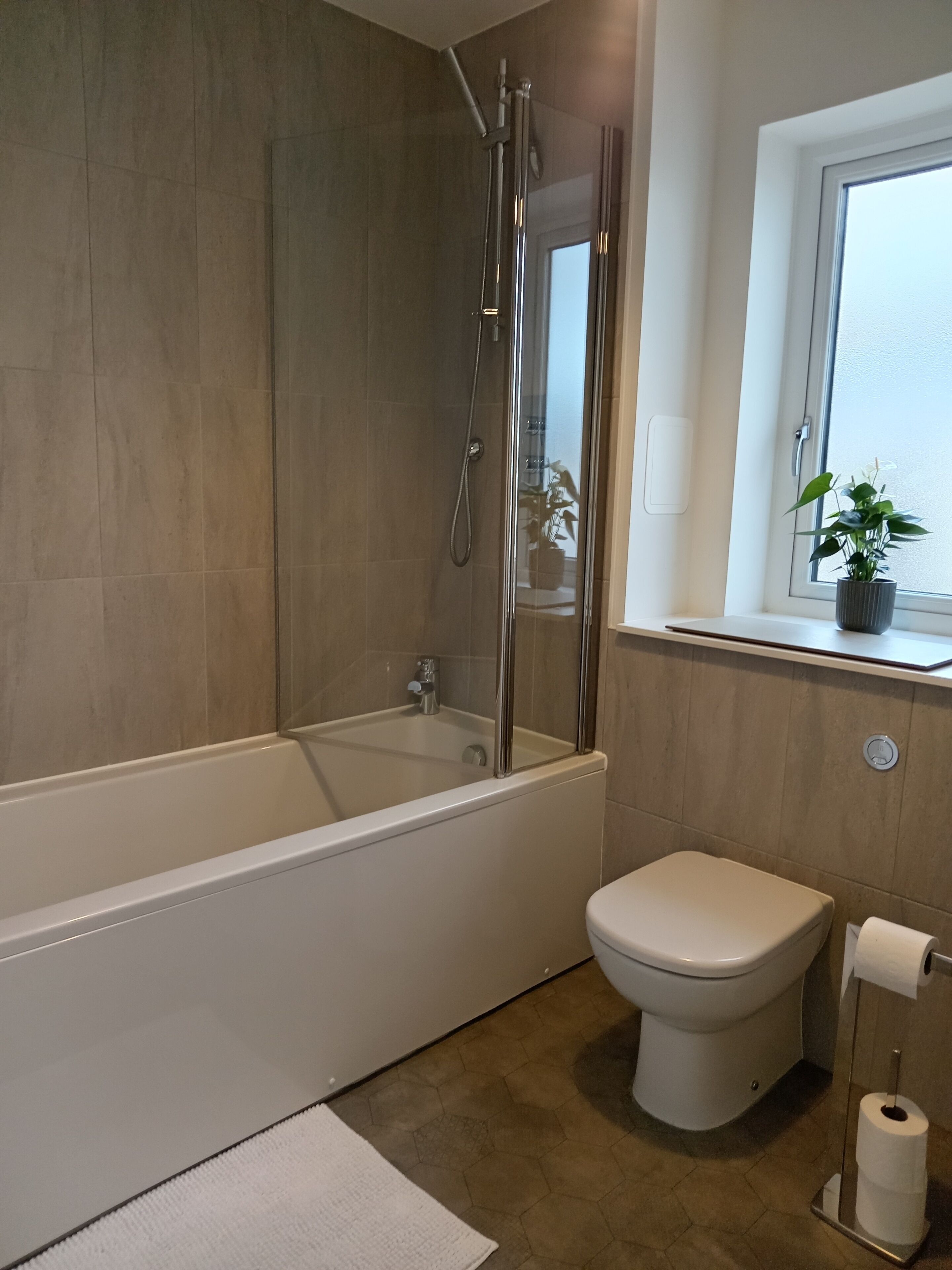 Ein modernes Badezimmer mit Badewanne, Toilette und einem Fenster mit Pflanze.