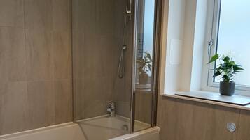 Ein modernes Badezimmer mit Badewanne, Toilette und einem Fenster mit Pflanze.