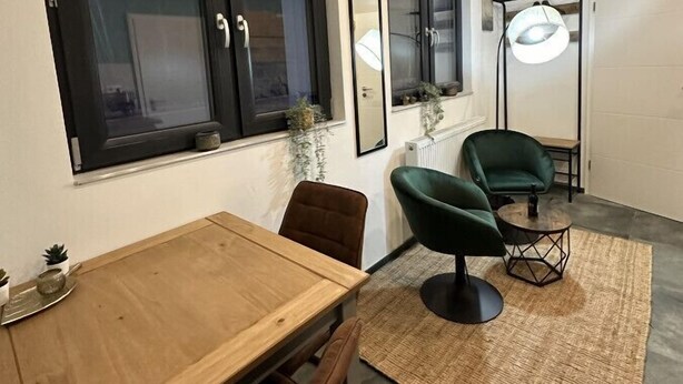 A modern dining area with a wooden table and chairs, a green upholstered chair, a floor lamp, and a large window with a view of the outside. - Relaxen im Weindorf Mayschoß Fewo 1 (Mayschoß)
