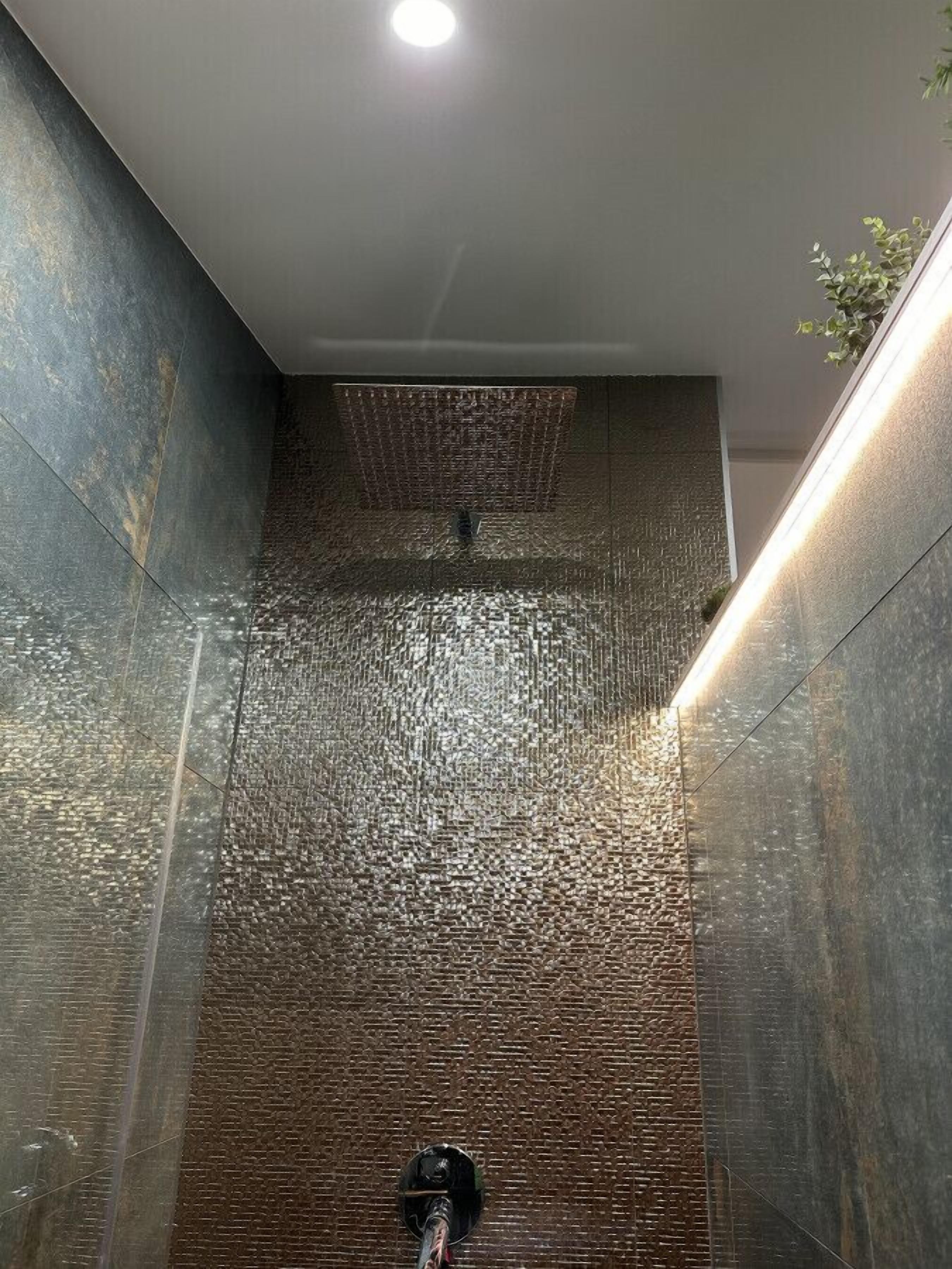 Une salle de bain moderne avec un mur texturé, un espace douche et un luminaire au plafond.