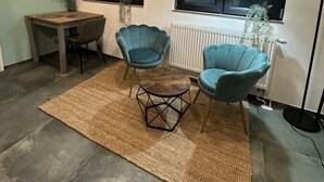 A modern living room with two blue armchairs, a wooden coffee table, a dining table with chairs, a floor lamp, and a view of the outdoors through large windows. - Relaxen im Weindorf Mayschoß Fewo 3 (Mayschoß)