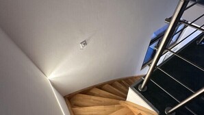 Een houten trap met een metalen leuning, witte muren en een kleine lamp.