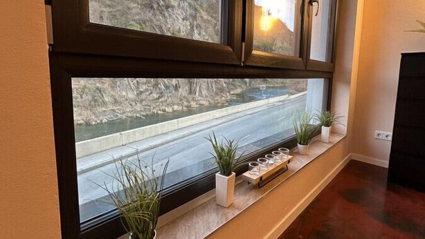 Een kamer met een groot raam dat uitkijkt over een rotsachtig landschap en een weg. Er staan bloempotten op de vensterbank.