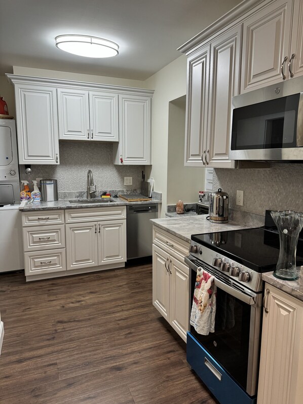 A modern kitchen with white cabinetry, a stainless steel dishwasher, a black stove, and a microwave above the counter.