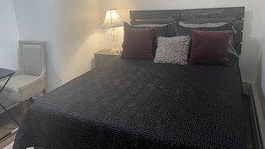 Une chambre à coucher bien rangée, avec un lit, une chaise, une table de chevet et une lampe fixée au mur.