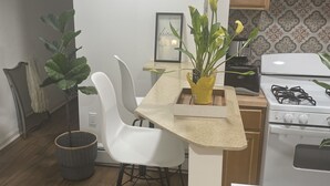 Une cuisine compacte avec des meubles blancs, une cuisinière à gaz, un évier et un coin repas avec des chaises blanches.