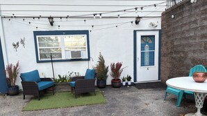 Une terrasse dotée de meubles en osier, de plantes en pot et d’une porte sur laquelle est inscrit « BIENVENUE ».