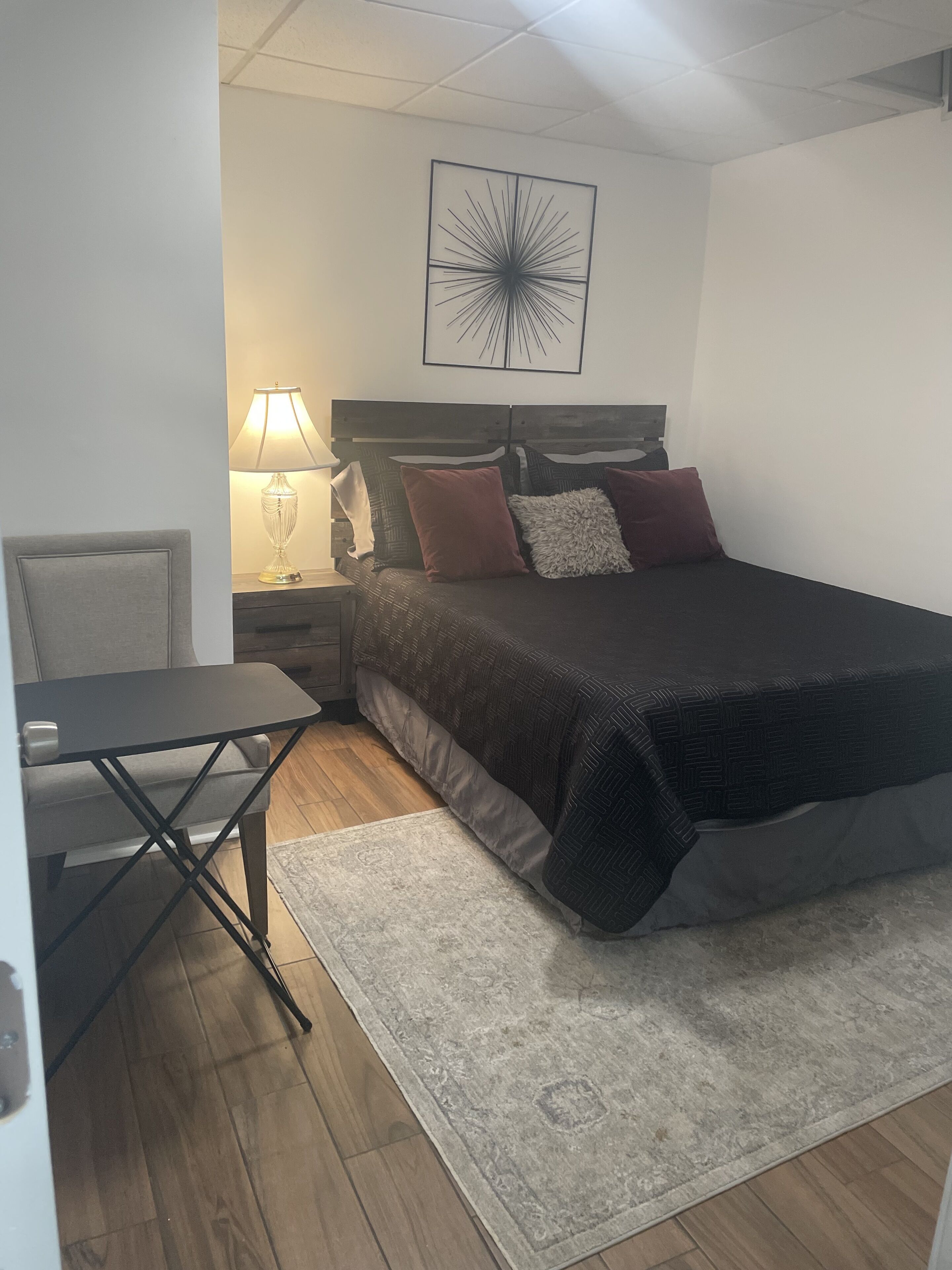 A bedroom with a bed, nightstand, lamp, chair, and a rug.