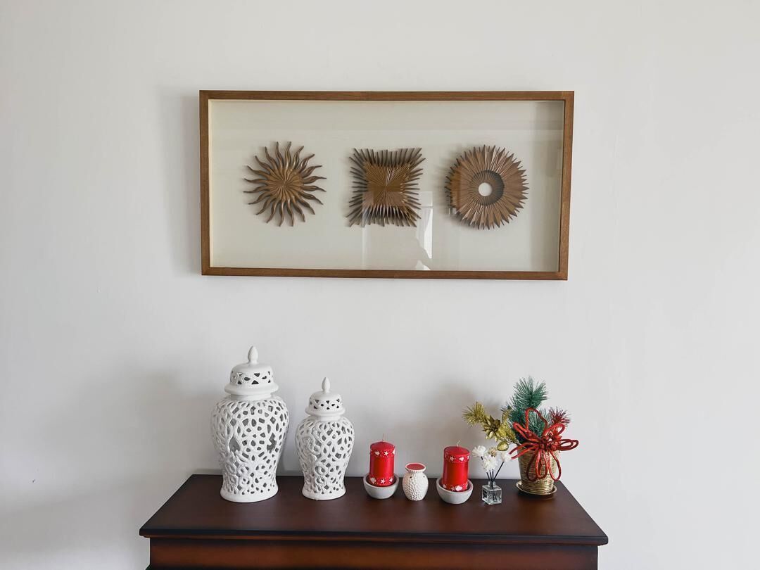 Une œuvre d’art encadrée représentant trois objets décoratifs sur un mur, une table en bois avec divers objets, dont des bougies blanches et rouges, et une petite plante.
