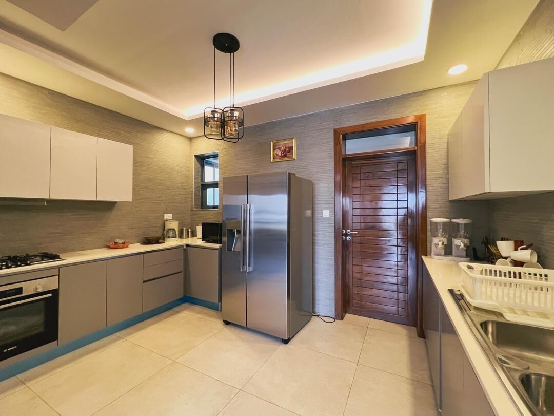 A modern kitchen with a built-in stove, stainless steel refrigerator, and a wooden door.