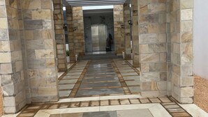 A corridor with stone walls and a tiled floor leading to a door.