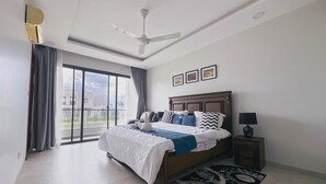 A modern bedroom with a large bed, a ceiling fan, and a view through a sliding glass door.