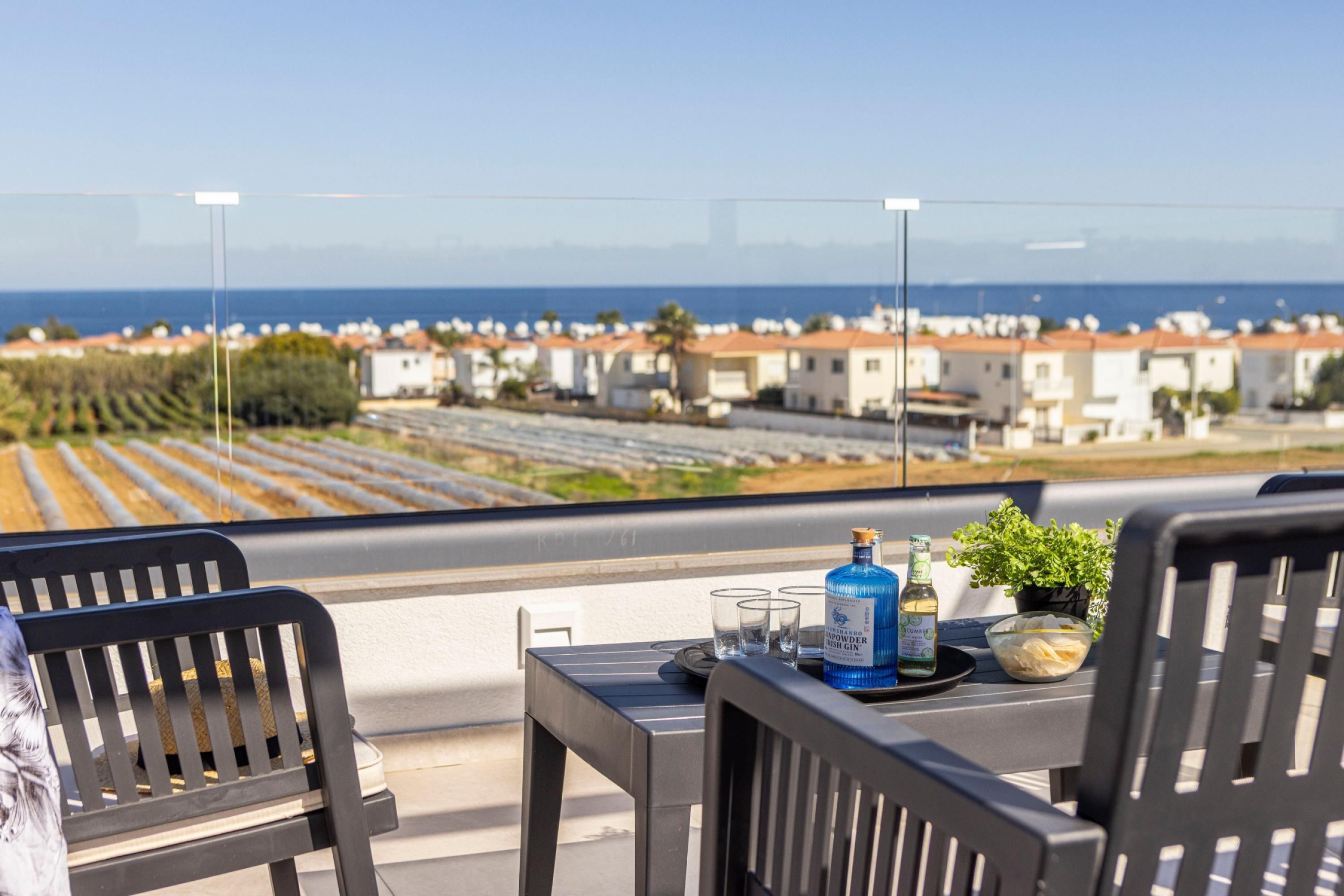 Un balcon avec une table dressée pour deux personnes, offrant une vue sur une ville côtière et des vignobles.