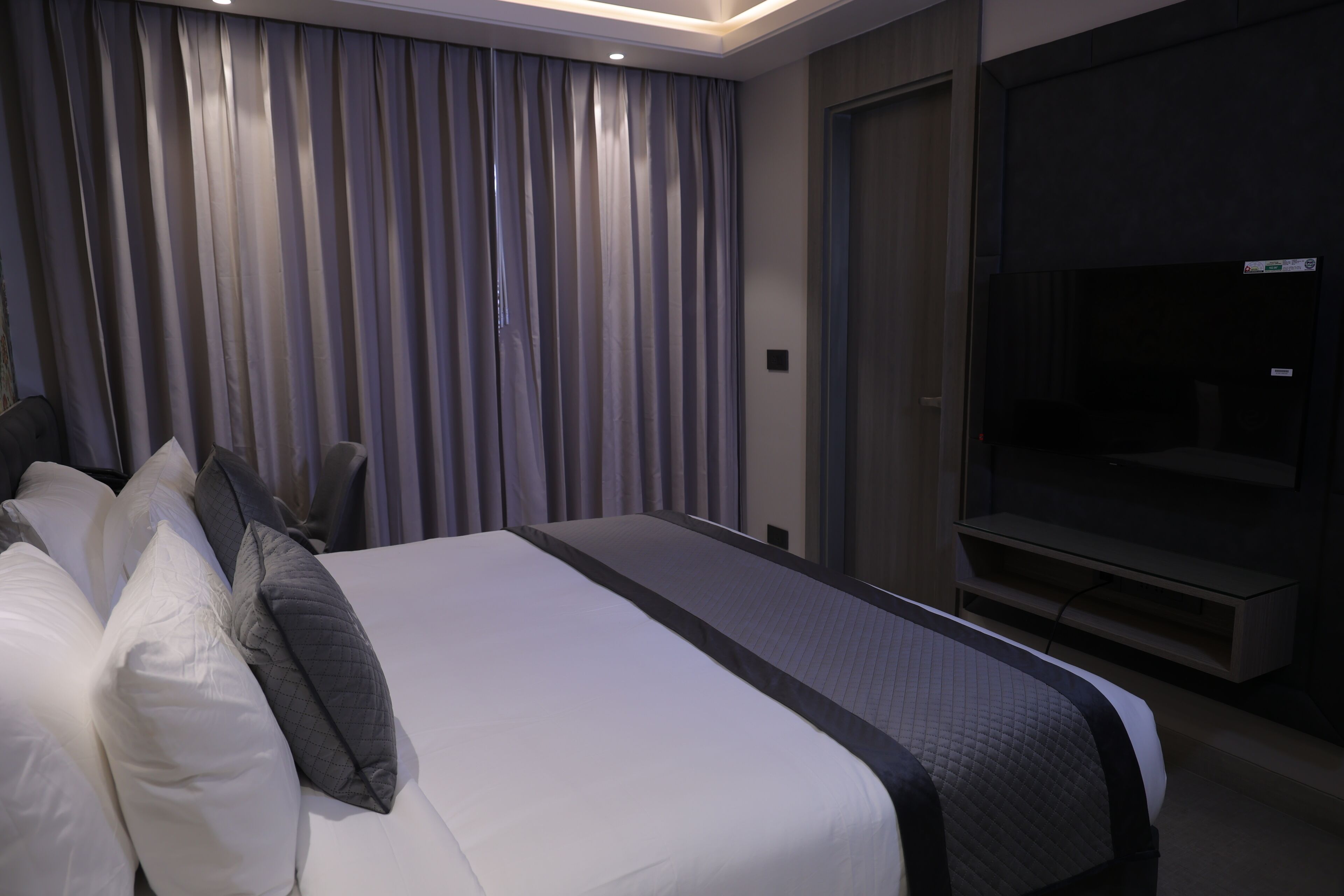 Una habitación de hotel moderna con una cama grande, un televisor de pantalla plana y un ventanal con cortinas.
