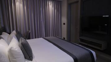 Una habitación de hotel moderna con una cama grande, un televisor de pantalla plana y un ventanal con cortinas.