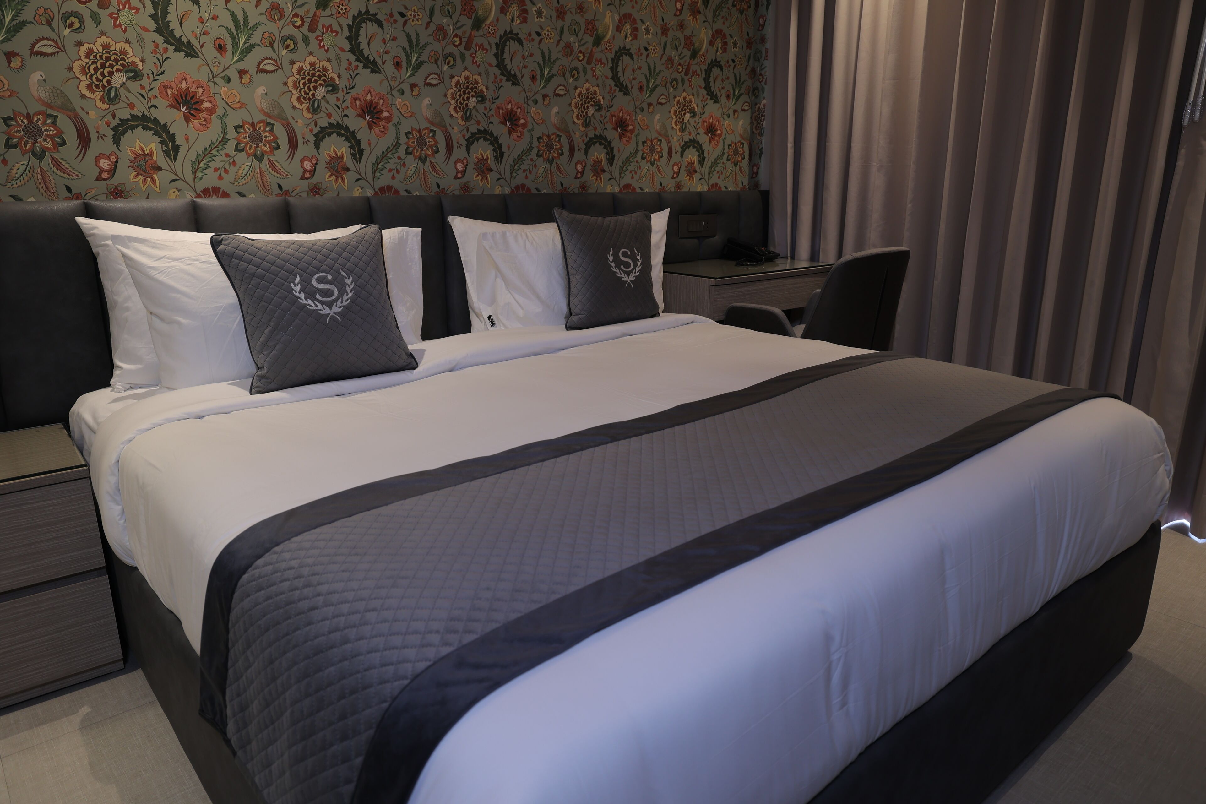 A neatly made bed with a dark headboard, a bedside table, and a chair.