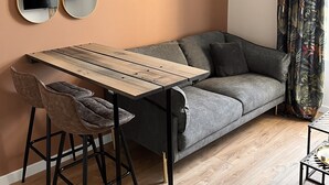 A modern living room with a wooden table, two chairs, a grey sofa, and a patterned curtain. - Appartement Douillet (Angoulême)