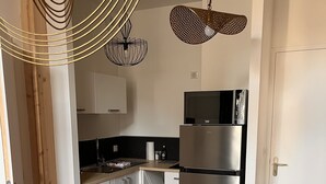 A modern kitchen with white cabinets, a stainless steel refrigerator, and a wooden dining table. - Appartement Douillet (Angoulême)