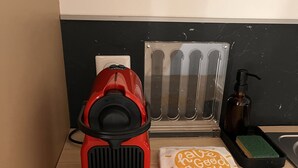 A red coffee maker, a tissue box, a bottle of hand soap, and a green sponge on a wooden surface. - Appartement Douillet (Angoulême)
