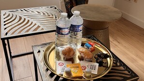 A room with a wooden floor, a metal table with a tray holding bottled water, bread, and a small box. - Appartement Douillet (Angoulême)