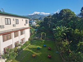 Un patio con vistas a montañas nevadas, rodeado de vegetación exuberante y un edificio con numerosas ventanas y unidades de aire acondicionado.