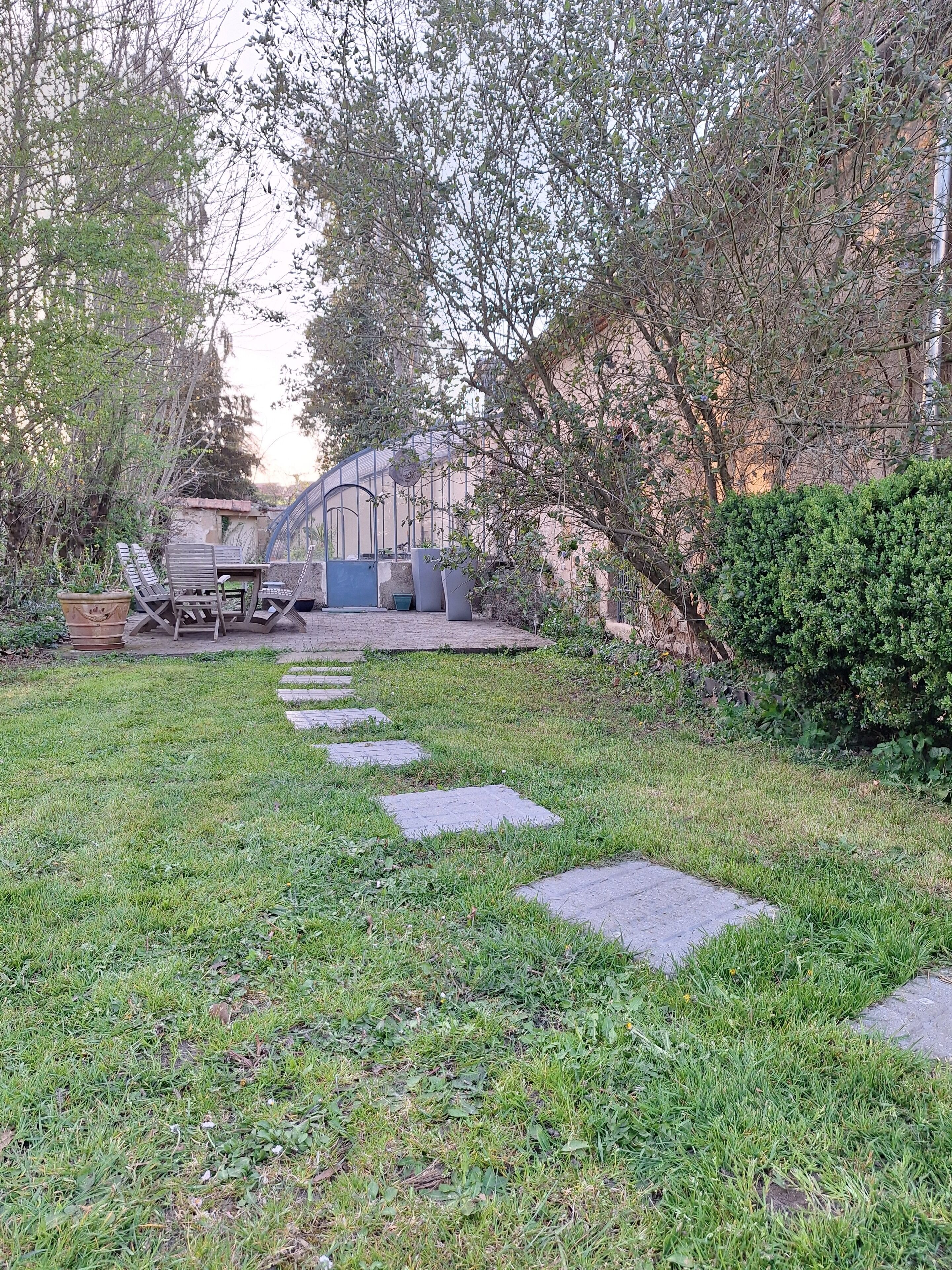 A garden with a paved pathway, outdoor furniture, and a greenhouse structure.