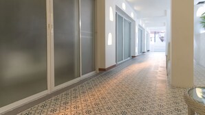 A hallway with patterned floor tiles, frosted glass doors, and a view of a staircase in the distance. - Windy Inn (Pattaya)