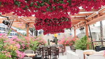 An indoor patio area with a patterned floor, wooden furniture, and hanging red flowers.