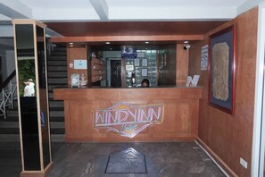 A reception desk with a neon sign, a staircase, and a wall with various notices.