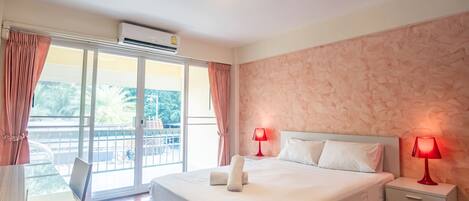 A hotel room with a large bed, two bedside tables with lamps, a window with curtains, and an air conditioning unit.