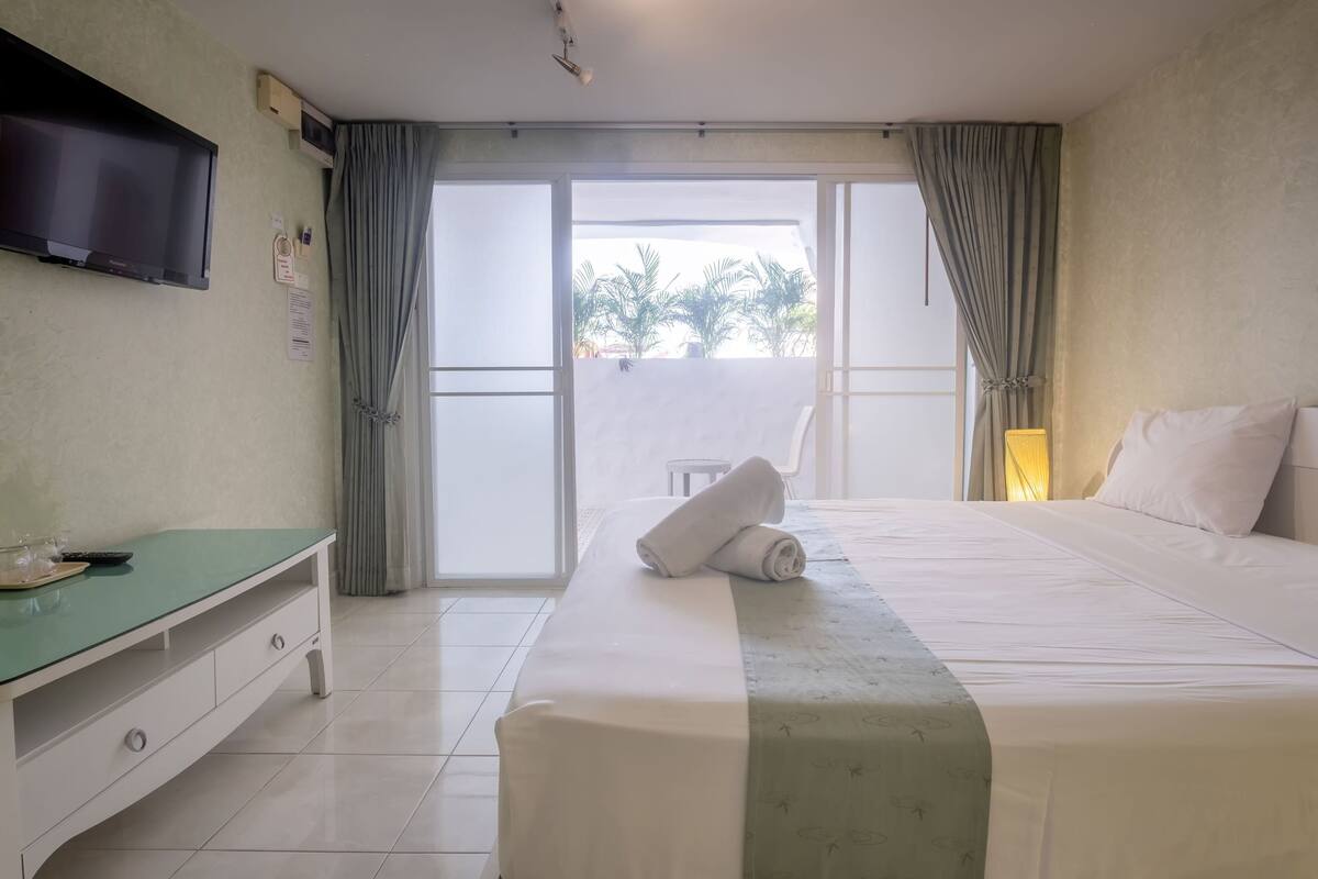 A hotel room with a bed, a TV mounted on the wall, a desk, and a view of the outdoors.