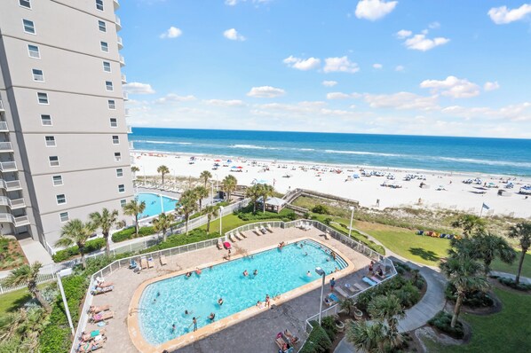 A hotel with a swimming pool, beach view, and a high-rise building.