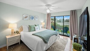 A bedroom with a bed, nightstand, lamp, and a view of a balcony.