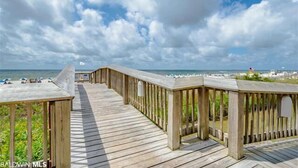 A wooden boardwalk leading to a beach with a clear view of the ocean and a partly cloudy sky.