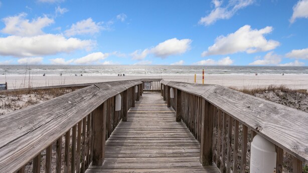 A wooden boardwalk leading to a beach with a clear sky.